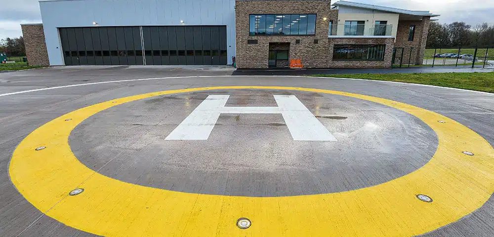 Aircraft helipad with a large white "H" symbol surrounded by a yellow circle at a modern building fa.
