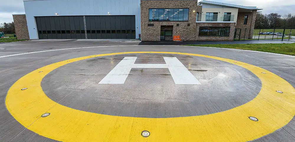 Aircraft helipad with a large white "H" symbol surrounded by a yellow circle at a modern building fa.